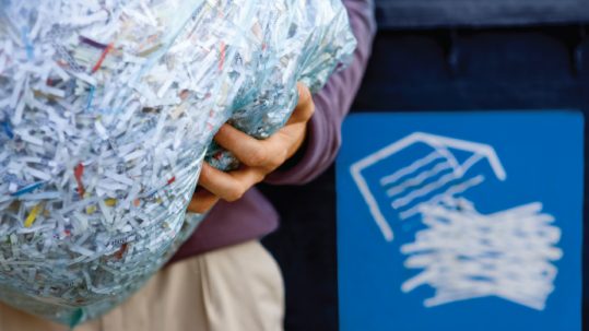 person holding bag of shredded paper going into a recycling bin
