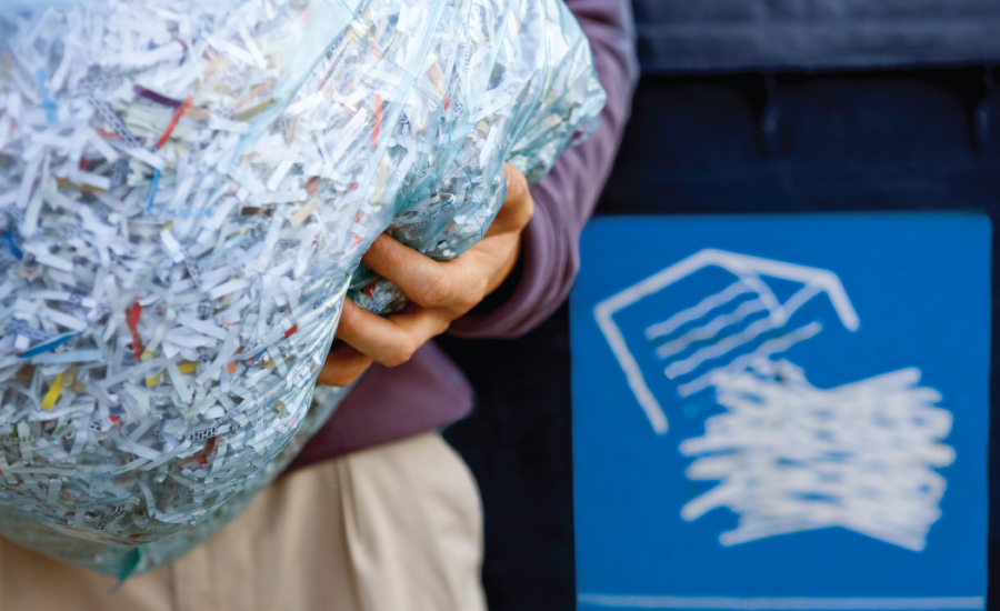 person holding bag of shredded paper going into a recycling bin