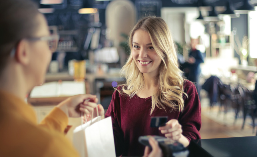 Young adult female at cash register paying for items with a debit card and smiling