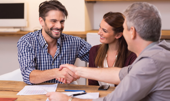 Young couple smiling and shaking hands with a friendly banker