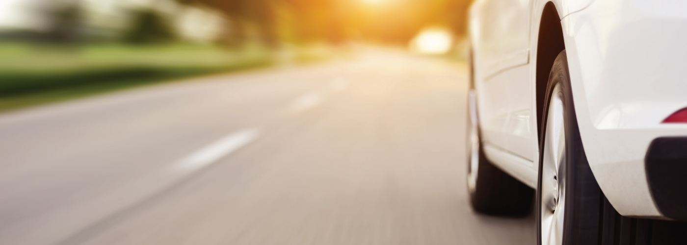 Decorative closeup of driver side of white sedan driving down road on sunny day