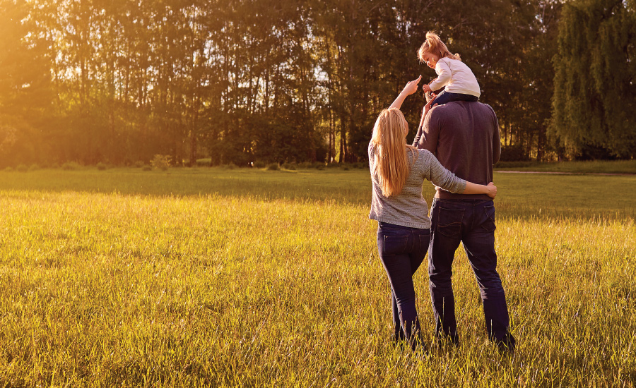 Husband and wife walk through wooded area with young daughter on father's shoulders