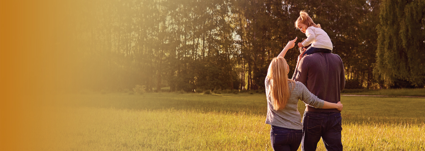 Husband and wife walk through wooded area with young daughter on father's shoulders