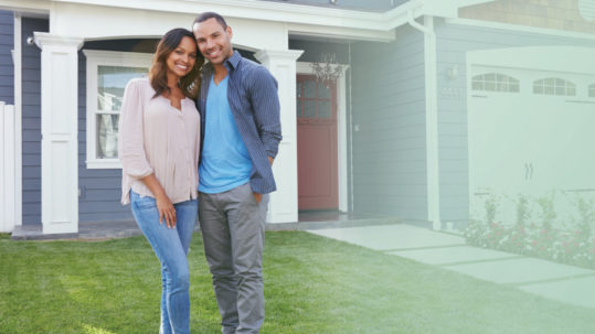 Young couple smiling in front of their newly purchased home